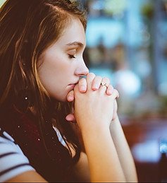 A worman with her hands clasped in fornt of her mouth and eyes closed.