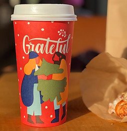red and multicolored grateful disposable cup with lid near pastry on table